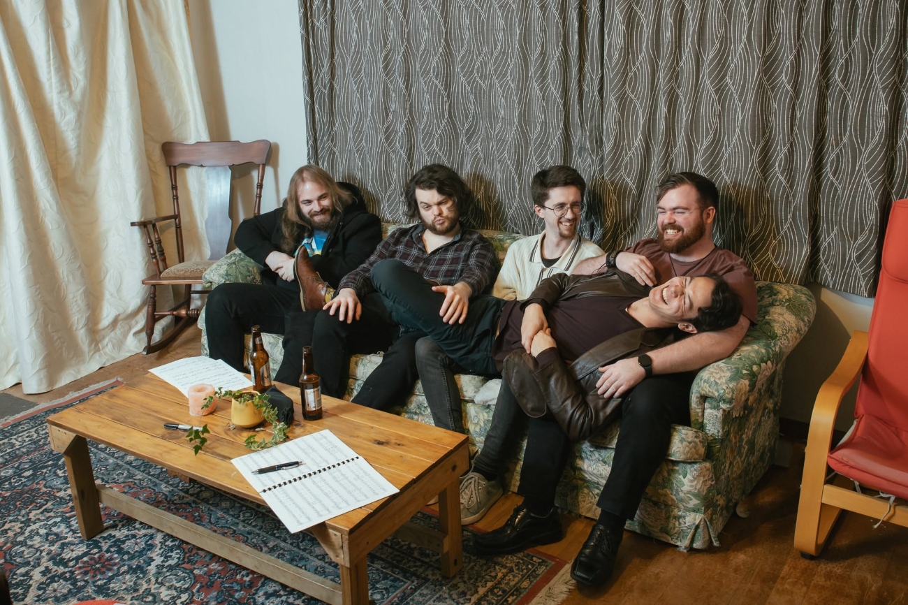 Deen lays across the laps of his band members seated on a couch